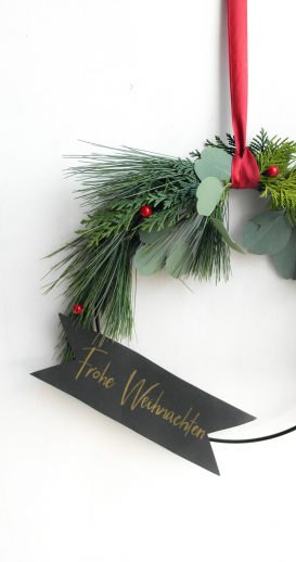 Hängender Kranz mit einem Banner und dem Wunsch" Frohe Weihnachten"